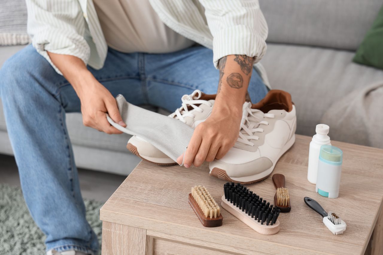 Entretien de sneakers en cuir bordeaux avec brosse douce, chiffon et crème nourrissante sur une table.