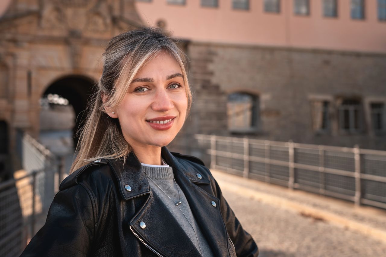 Jeune femme souriante en trench, sneakers claires, dans une rue bordelaise aux façades en pierre